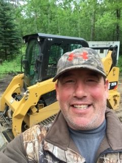 A man in camouflage hat standing next to a yellow cat.